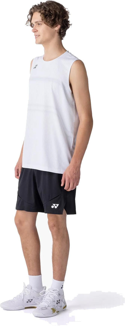 A young man smiles, wearing Yonex 15239YX Knit Men's Padel Shorts in black with a white sleeveless top, white socks, and sneakers. He stands slightly turned right against a plain white background.