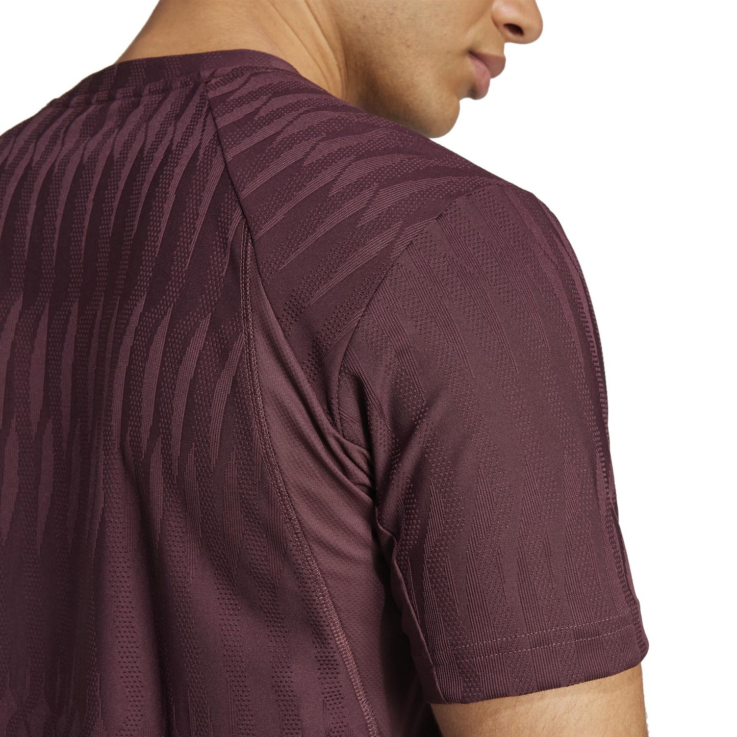 A person in the adidas ADIDAS Mens Climacool+ Freelift Padel T-Shirt - Ruby, made from recycled materials, stands sideways. The focus is on the upper back and shoulder area, showcasing the innovative blend of function and eco-friendly fabric.