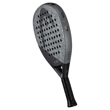 The HEAD Vibe 2025 Padel Racket in grey and black boasts an oversized teardrop shape with a patterned surface, multiple perforations, and a Power Foam core. "VIBE" is printed on the racket head and complemented by the black handle.