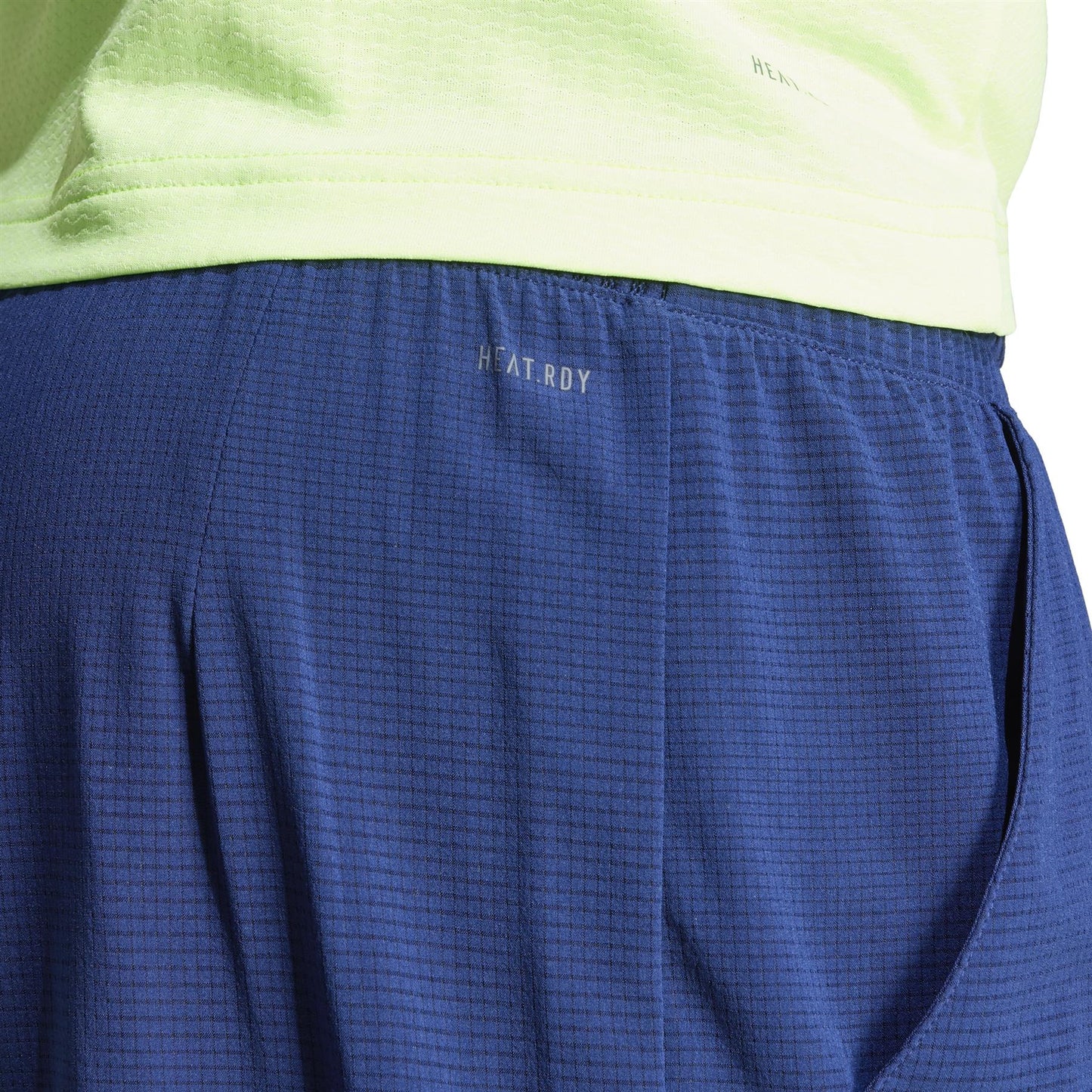 Close-up of a person wearing navy ADIDAS Ergo Mens Padel Shorts and a light green top. The shorts display "HEAT.RDY" near the waistband, are crafted from recycled materials, and feature a textured, breathable fabric.