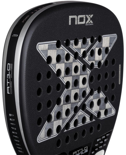 Close-up of the NOX Luxury AT10 Genius Attack 18K Alum By Agustin Tapia 2026 padel racket, with a checkered center, X-shaped holes, and textured black surface in aluminised carbon. Brand and model names are prominently displayed.