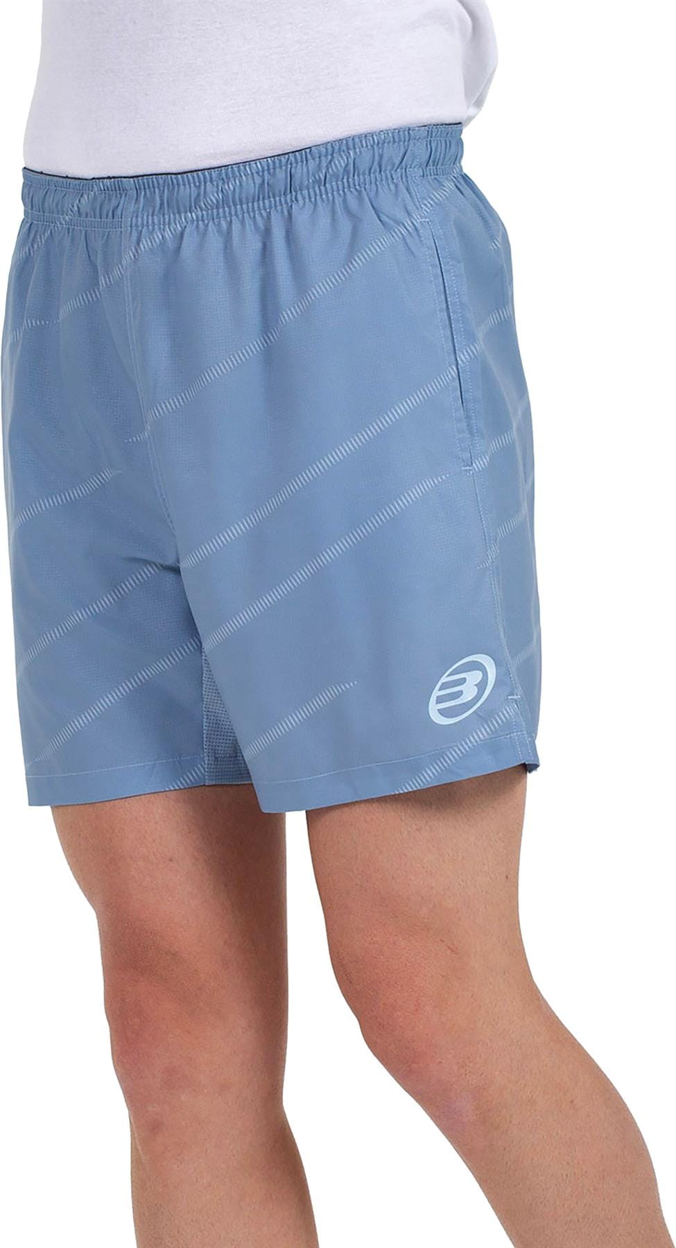 A person stands against a plain background, showing only the lower torso and upper legs, wearing Bullpadel Cabanas Mens Padel Shorts in Shadow Blue—featuring a small white logo and Quickerdry technology for padel court performance.