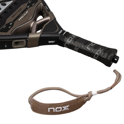 Close-up of the handle and wrist strap of the NOX AT10 Pro Cup Hard By Agustín Tapia 2026 padel racket, showing a black textured grip and detachable brown and beige strap with the NOX logo.