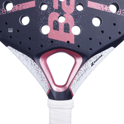 Close-up of the Babolat Stima Spirit Padel Racket, featuring a lightweight design in black and coral. The racket showcases perforations and geometric patterns, with the handle wrapped in white grip tape for optimal maneuverability. A triangular cutout near the base adds a distinct design element.