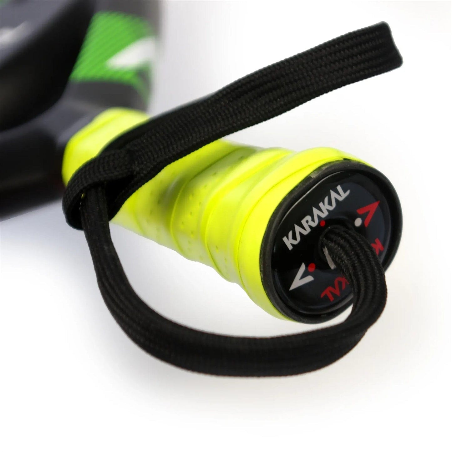 Close-up of the Karakal Air Lite 345 Green Padel Racket handle with a black wrist strap. The end cap shows the Karakal logo and red and white arrows, while the lightweight frame has green and black accents.
