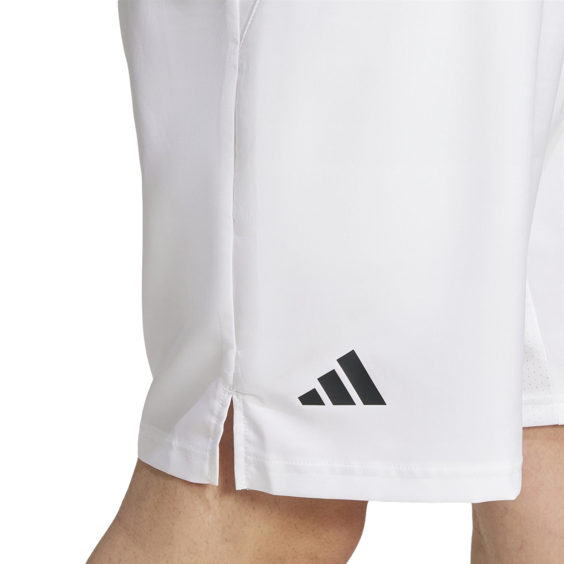 Close-up of a person wearing ADIDAS Men's 3 Stripe Padel Shorts in white, highlighted by a small black adidas logo on the left leg. These moisture-wicking shorts feature a subtle side slit at the hem, ideal for comfort and style during intense games.