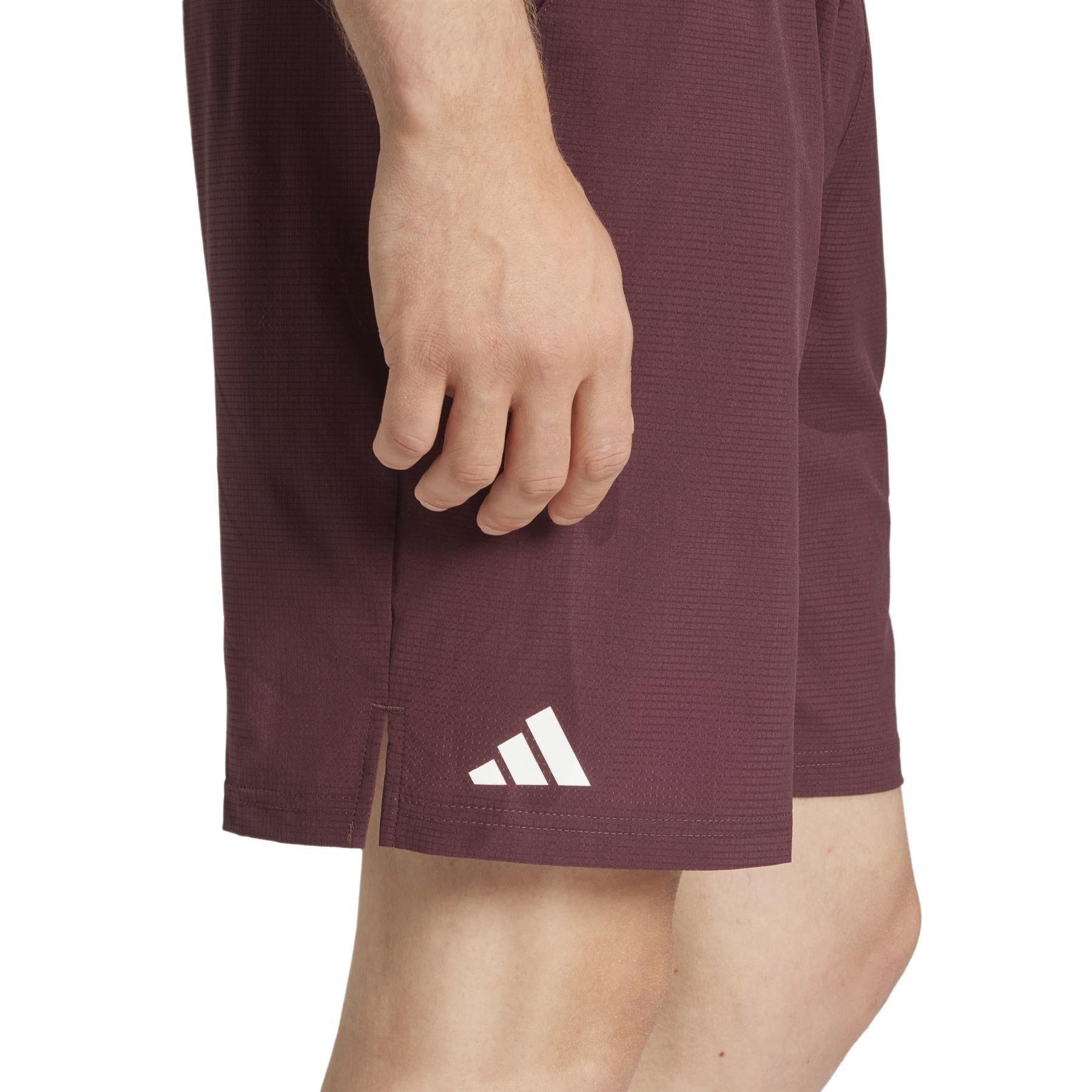 A person wearing Ruby ADIDAS Ergo Men's Padel Shorts with a small white geometric logo showcasing three diagonal stripes on the side. Made from recycled materials, these shorts feature HEAT.RDY technology for cool comfort. The image highlights the shorts' side view.