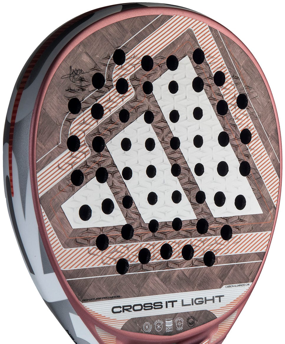 A close-up of the adidas Cross It Light 2026 Padel Racket in white and pink, featuring a carbon fibre frame, geometric pattern, round perforations, textured surface, and the adidas logo near the bottom of the face.