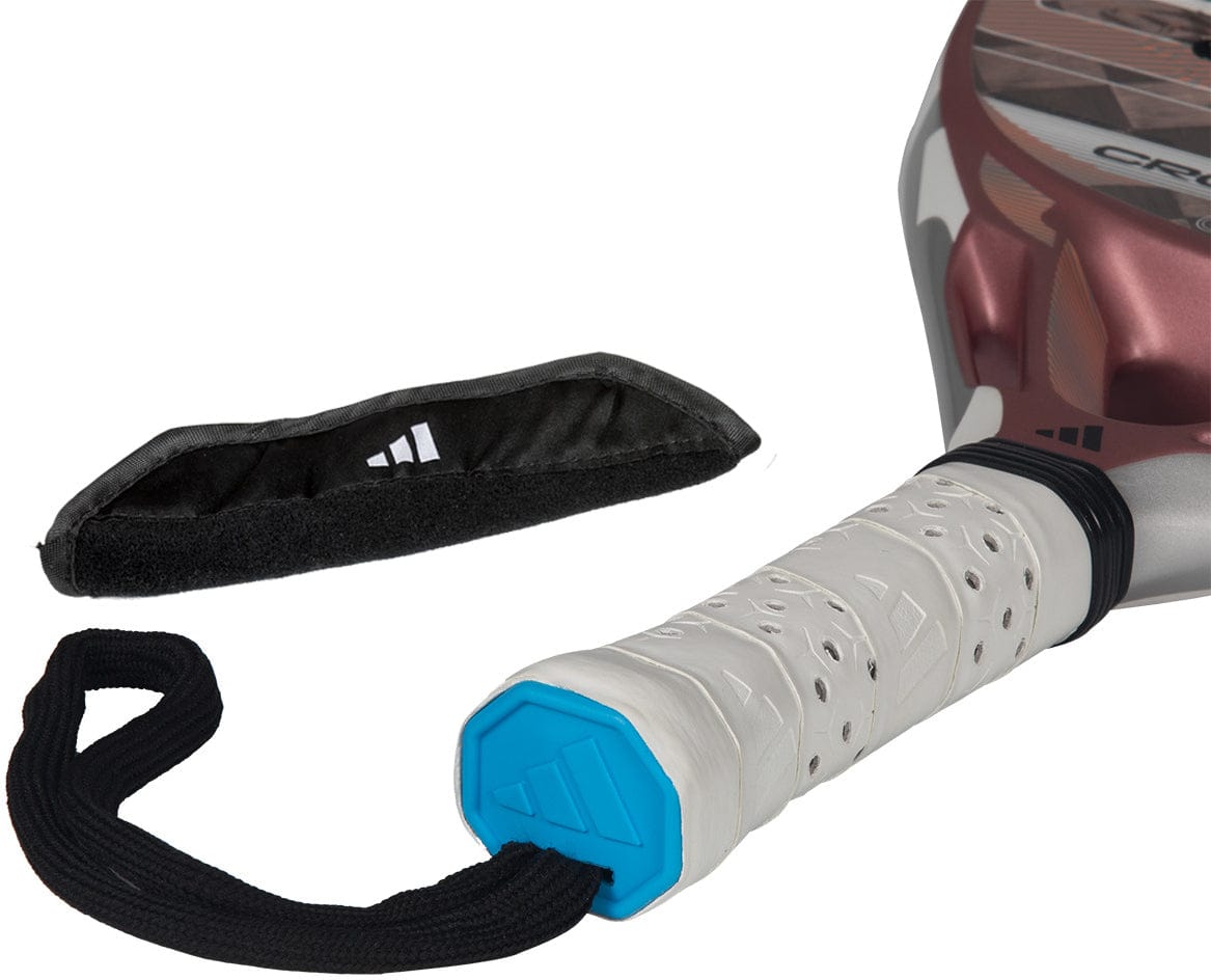 A close-up of the adidas Cross It Light 2026 Padel Racket - White / Pink shows its handle with a white grip, blue end cap, black wrist strap, and detached black Velcro strap cover featuring a small white logo.