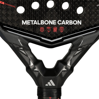 Close-up of the adidas Metalbone Carbon 2026 padel racket for advanced players, with “METALBONE CARBON” on the face, red icons, circular holes, carbon fiber texture, and the adidas logo on the neck.