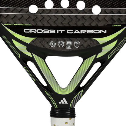 Close-up of the adidas Cross It Carbon 2026 Padel Racket in Black/Green, an advanced carbon fibre racket with a triangular throat, textured surface, and "Cross It Carbon" branding plus technical icons.