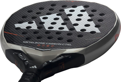 Close-up of the adidas Metalbone Carbon CTRL 2026 padel racket for advanced players, showcasing a round hole pattern, textured surface, geometric design, and "METALBONE CARBON CTRL" branding.