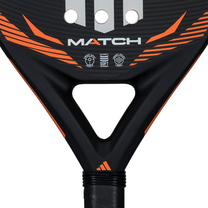 Close-up of the adidas Match Black 2026 Padel Racket - Black / Orange, a beginner padel racket with fibreglass construction, featuring "MATCH" in white, three vertical stripes above, and icons for "soft" and "level" features below.