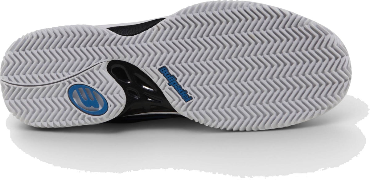 The image shows the white zig-zag sole of Bullpadel Indiga 26I Mens Padel Shoes - Black, featuring a blue circular logo and black heel section with “Bullpadel” branding—ideal for beginner padel players.