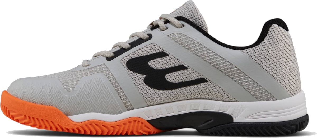 The Bullpadel Indiga 26I Mens Padel Shoes - Orange feature a light gray mesh upper, black logo and heel, white midsole, and a bright orange herringbone outsole with secure lace-up closure.