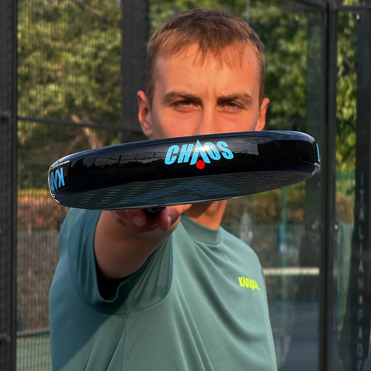A man holds a Karakal Chaos Dynamic 2026 padel racket toward the camera, showing the “CHAOS” logo on its edge.