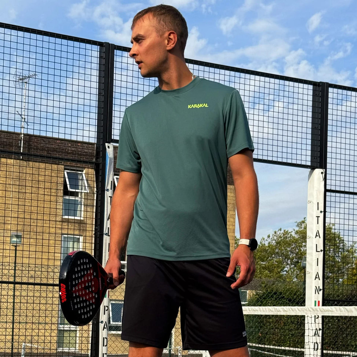 A man standing on a padel court holding a black and red Karakal Chaos Shredder 2026 Padel Racket.