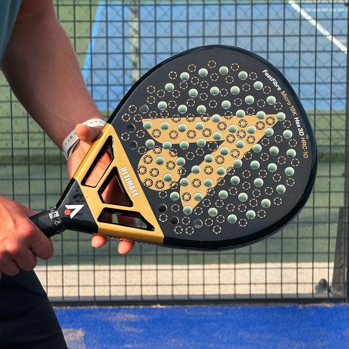 A person holds a black and gold Karakal Chaos Ultimate 2026 padel racket, featuring a triangular pattern and circular perforations on the 18K carbon graphite face.