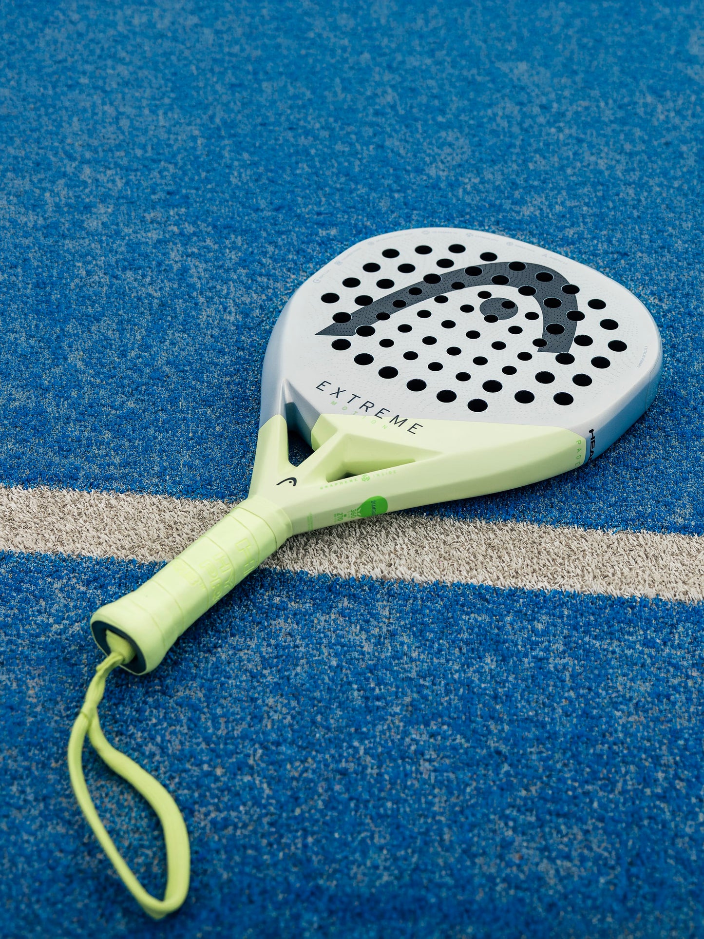 A pale green and gray HEAD Extreme Motion 2026 Padel Racket featuring “EXTREME” text rests on a blue textured court near a white boundary line—an ideal power padel racket from HEAD, designed for advanced players.