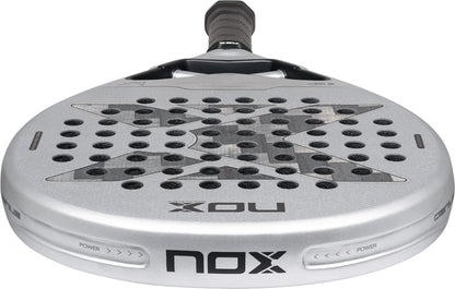 A silver and black NOX AT10 Genius 12K Alum Xtrem By Agustín Tapia 2027 padel racket with a teardrop shape, a perforated face, and a centered x-pattern.