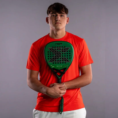 A young man in a red t-shirt holds a green and black NOX Ventus Attack 12K Xtrem By Aimar Goñi 2027 padel racket.