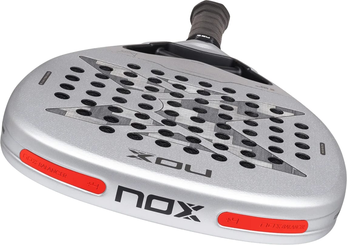 Silver teardrop-shaped NOX AT10 Genius Attack 12K Alum Xtrem By Agustín Tapia 2027 padel racket with a textured surface, numerous perforations, and two red balance weight inserts on the sides.