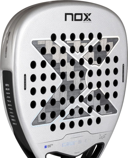 Silver-toned NOX AT10 Genius Attack 12K Alum Xtrem By Agustín Tapia 2027 padel racket featuring a large grey and black checkered X design, circular perforations on the hitting surface, and technical specification icons along the left edge.