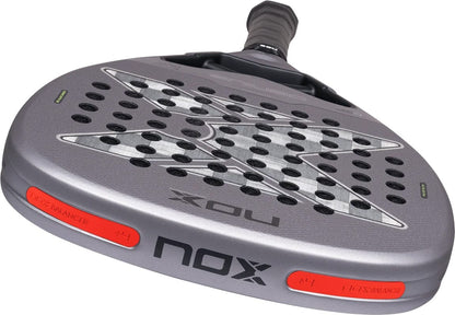 Grey NOX AT10 Genius Attack 18K Alum By Agustín Tapia 2027 padel racket with a textured, perforated hitting surface and orange weight inserts at the base of the frame.