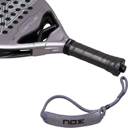 Gray diamond-shaped NOX AT10 Genius Attack 18K Alum By Agustín Tapia 2027 padel racket with a perforated black grip and a detachable wrist strap featuring a logo.