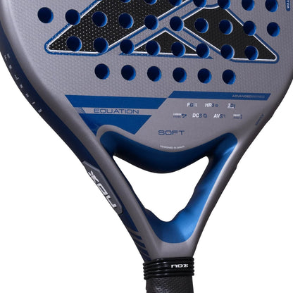 Close-up of a grey and blue NOX Equation Soft Advanced 2027 padel racket with a perforated face, featuring printed technical specifications and text including “EQUATION” and “SOFT.”