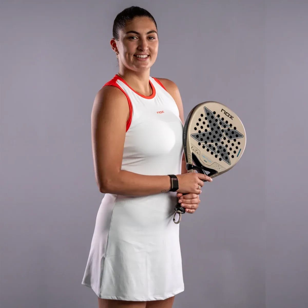 A female athlete in a white athletic dress holds a NOX Ventus Hybrid 12K Lite 2027 padel racket.