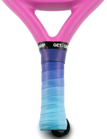 Close-up of a tennis racquet handle wrapped with the Get A Grip Padel Overgrip - Wavy, a gradient overgrip fading from dark blue to light blue. The pink frame displays a black "GET A GRIP" band. Brand: Get A Grip.