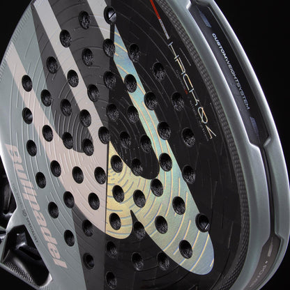 Close-up of the Bullpadel HACK 04 2026 Padel Racket in black and grey, showcasing its perforated surface, dynamic power design, detailed Bullpadel branding, and graphics against a dark background.