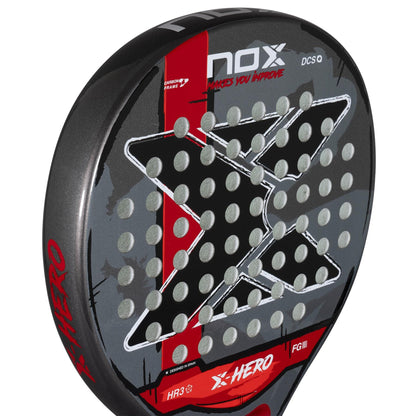 A close-up of the NOX X-Hero Red Padel Racket by NOX, designed for beginners, showcases its black, red, and gray color scheme with a large stylized "X" and multiple circular holes for improved control and precision.