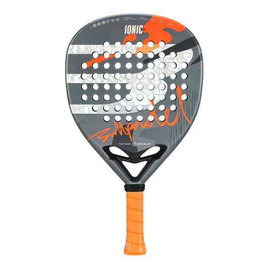 The Bullpadel Ionic Power 2025 Padel Racket features a sleek black and gray design with white diagonal stripes, vibrant orange accents, and an XFORCE System for enhanced performance. The "IONIC" branding is prominent, and the handle offers a bright orange grip tape for comfort.