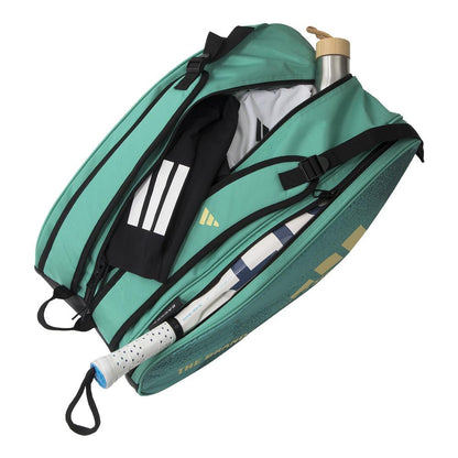 The ADIDAS Control 3.4 Padel Racket Bag - Green is open, revealing a tennis racket, a wooden-capped water bottle, and a black and white sports towel. Designed for court accessories, it features multiple compartments and a comfortable shoulder strap.