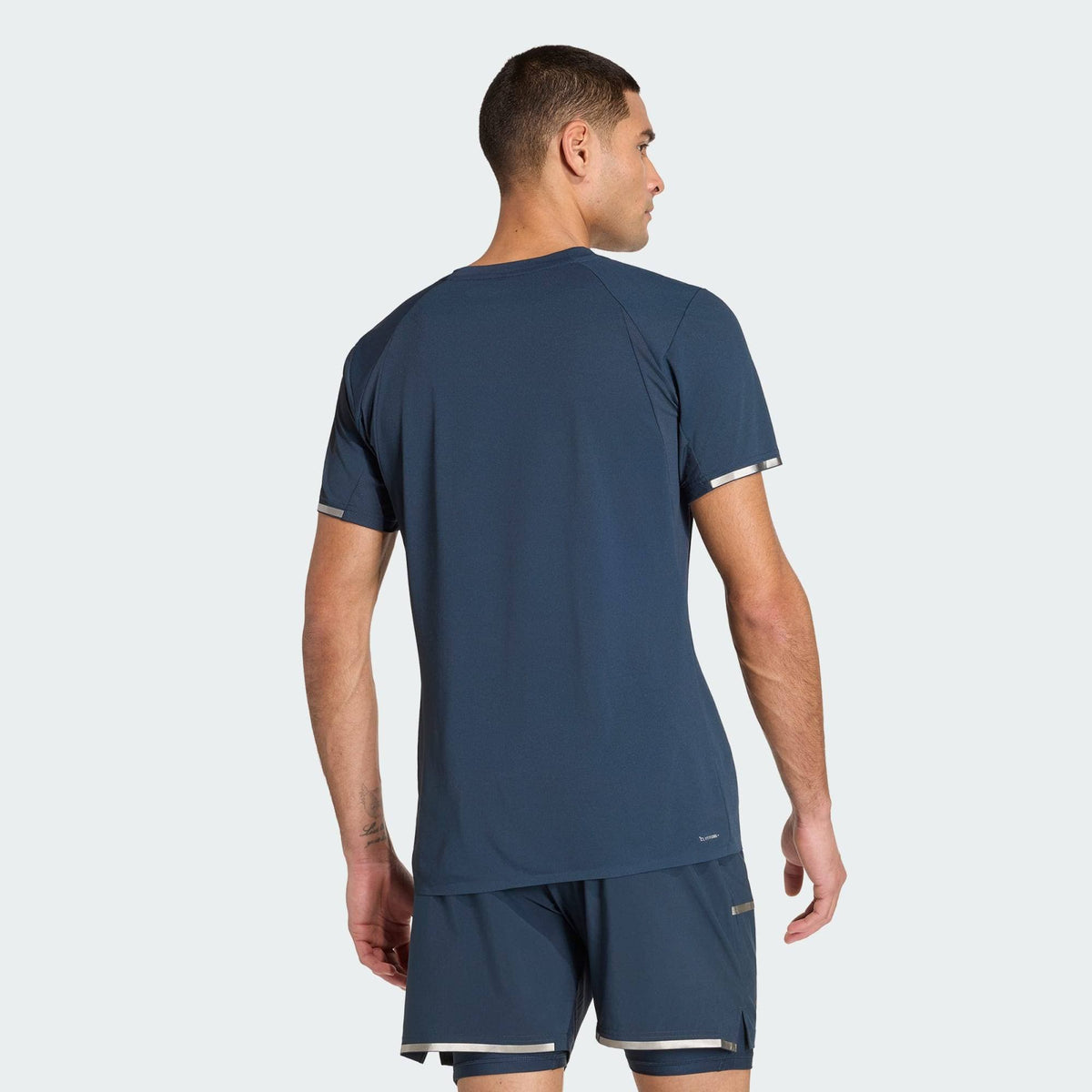 A man in an ADIDAS Climacool+ Freelift Pro Mens Padel T-Shirt - Aurora Ink and matching shorts stands with his back to the camera against a plain light background.