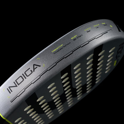 Close-up of the Bullpadel Indiga Ctr 2026 padel racket’s gray edge labeled "INDIGA," showing its specs for precision control—composition, weight, and balance—printed on the surface against a black background.