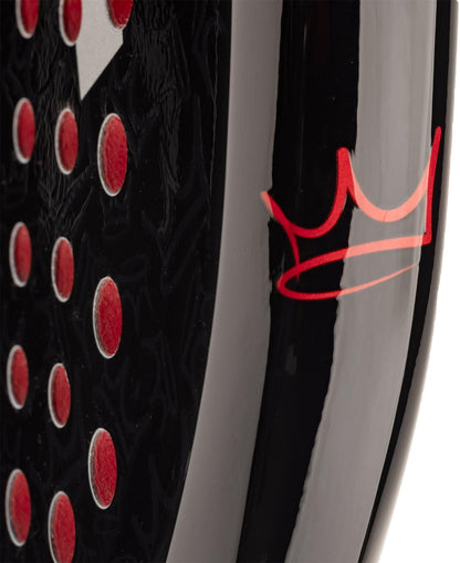 Close-up of the HEAD Coello Team 2025 Padel Racket - Black, showing red circular indents and a stylized red crown. Its glossy surface highlights advanced Power Foam construction by HEAD.