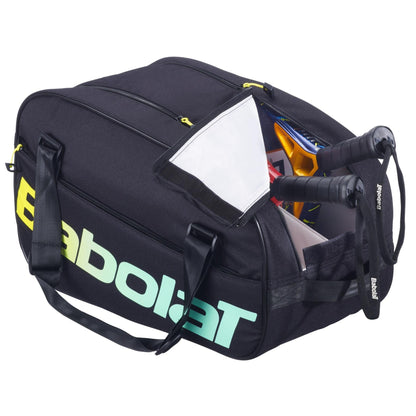 A Babolat Court S Padel Racket Bag - Black / Multi is partially unzipped, showing two rackets inside. It features the Babolat logo in white and green, black carry handles, and yellow zipper pulls.