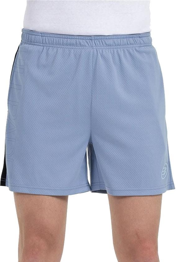 A person wearing Bullpadel Campaza Men's Padel Shorts in Shadow Blue with an elastic waistband and Quickerdry tech, paired with a white shirt, shown from waist to mid-thigh.