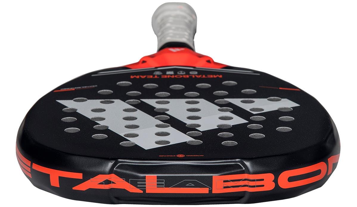 A close-up of the adidas Metalbone Team 2026 Padel Racket - Black / Red displays its black frame, bold white logo, red accents, Spin Blade Gritt tech, white grip tape, and "METALBONE" partially shown on the rim.