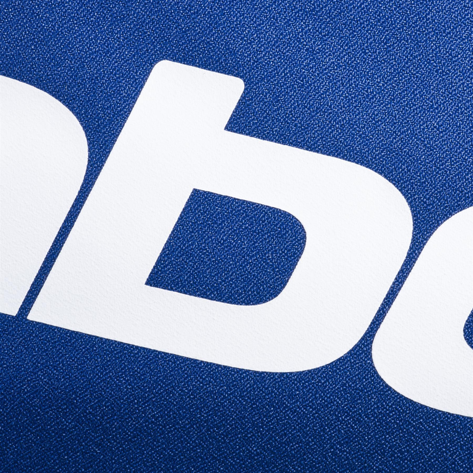 Close-up of bold, white lowercase "b" and part of "d" on a textured dark blue background, likely from the Babolat logo on the Babolat Court S Padel Racket Bag - Dark Blue, a stylish padel equipment bag by Babolat.