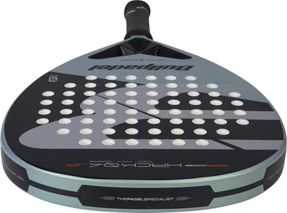 A close-up of the Bullpadel HACK Junior 2026 Padel Racket shows its black handle, grey and black face with white holes, and bold Bullpadel branding inspired by Paquito Navarro's racket on the front and edges.