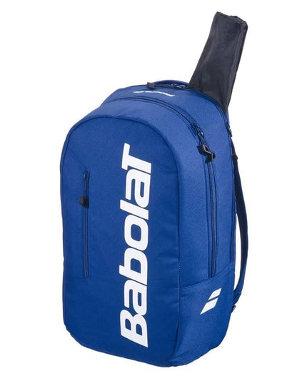 The Babolat Court Lite Padel Backpack in dark blue features white branding and a zippered racket compartment, with only the tennis racket’s handle visible outside the bag.