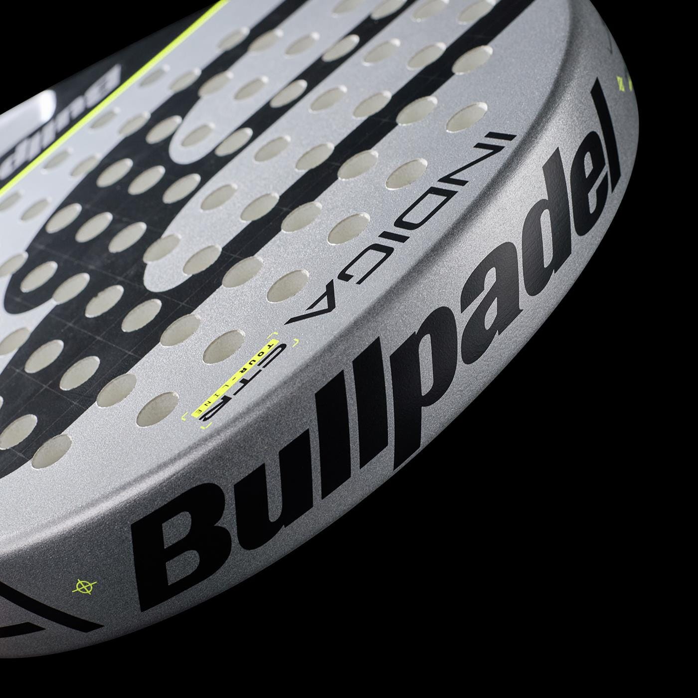 Close-up of a grey Bullpadel Indiga Ctr 2026 padel racket featuring bold black Bullpadel branding and circular perforations for precision control, displayed against a black background.