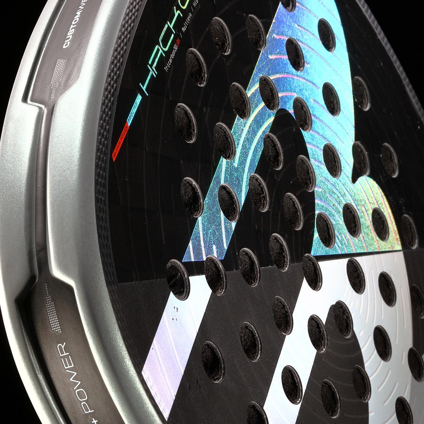 Close-up of the Bullpadel HACK 04 2026 Padel Racket by Bullpadel in black and grey, highlighting its reflective, colorful design, dynamic power, multiple round holes, and edge details labeled "+Power" and "Custom Weight.