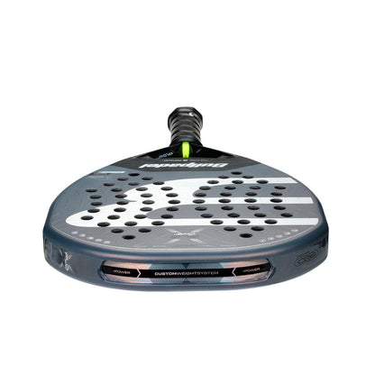 A close-up of the Bullpadel XPLO Comfort 2026 Padel Racket - Grey shows its black, gray, and silver design with multiple face holes and "Custom Weight System" branding near the handle for comfort and explosive power.