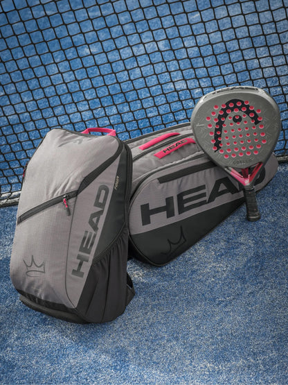 Two HEAD Tour Padel Racket Bag L - Coello bags in gray and black sit on a blue court next to a black and pink padel racket, with the net in the background.