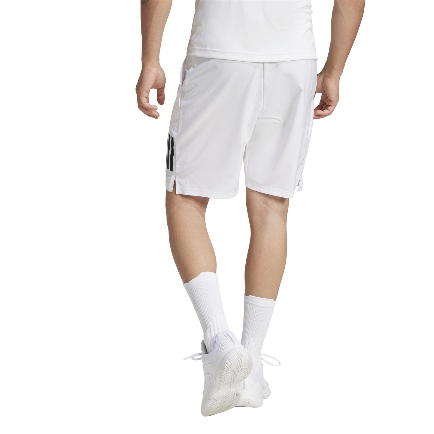 A person in ADIDAS Men's 3 Stripe Padel Shorts - White, complete with a white shirt, white sneakers, socks, and the black-striped shorts is walking away against a plain white background.